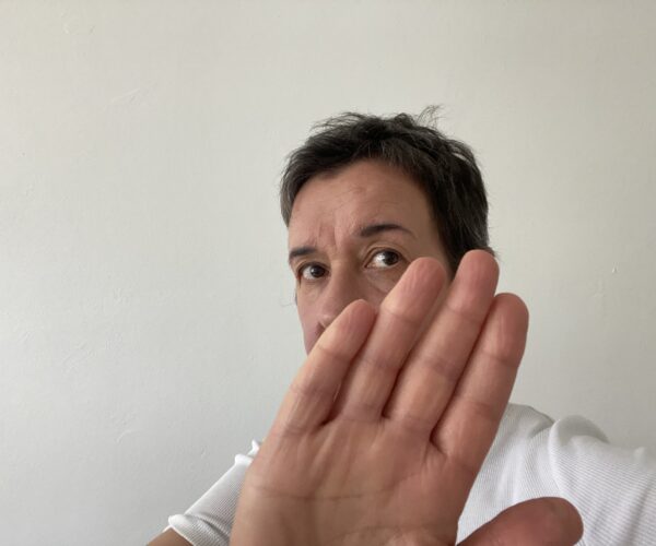 Person zeigt mit der Hand Stopp und verdeckt dabei ihr Gesicht teilweise.